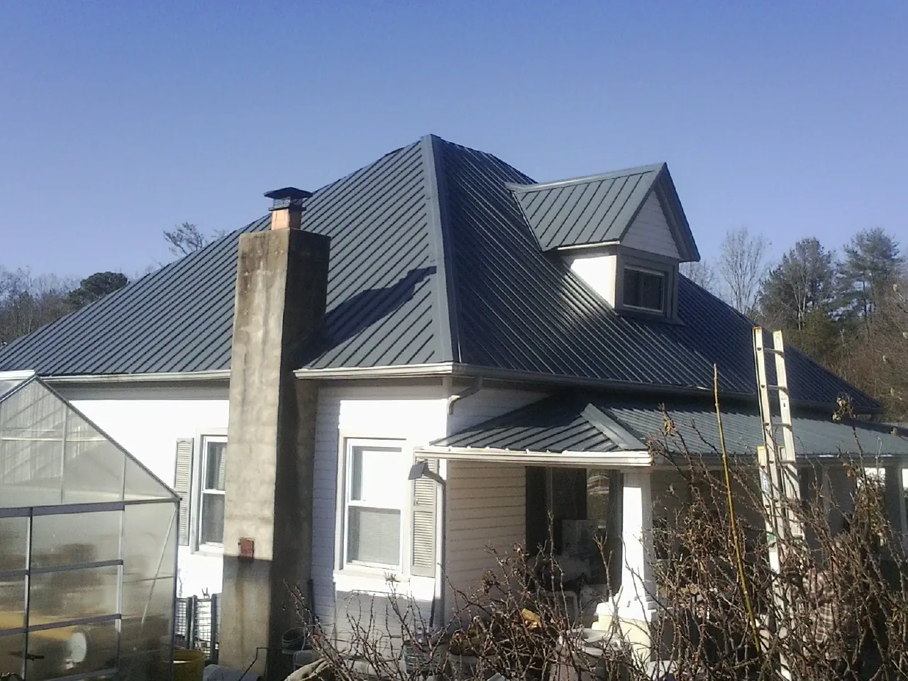 Dark blue standing seam metal roof on a white farmhouse with dormer — Slate & Tile Roof Repair by Roofing Brothers in Parkville