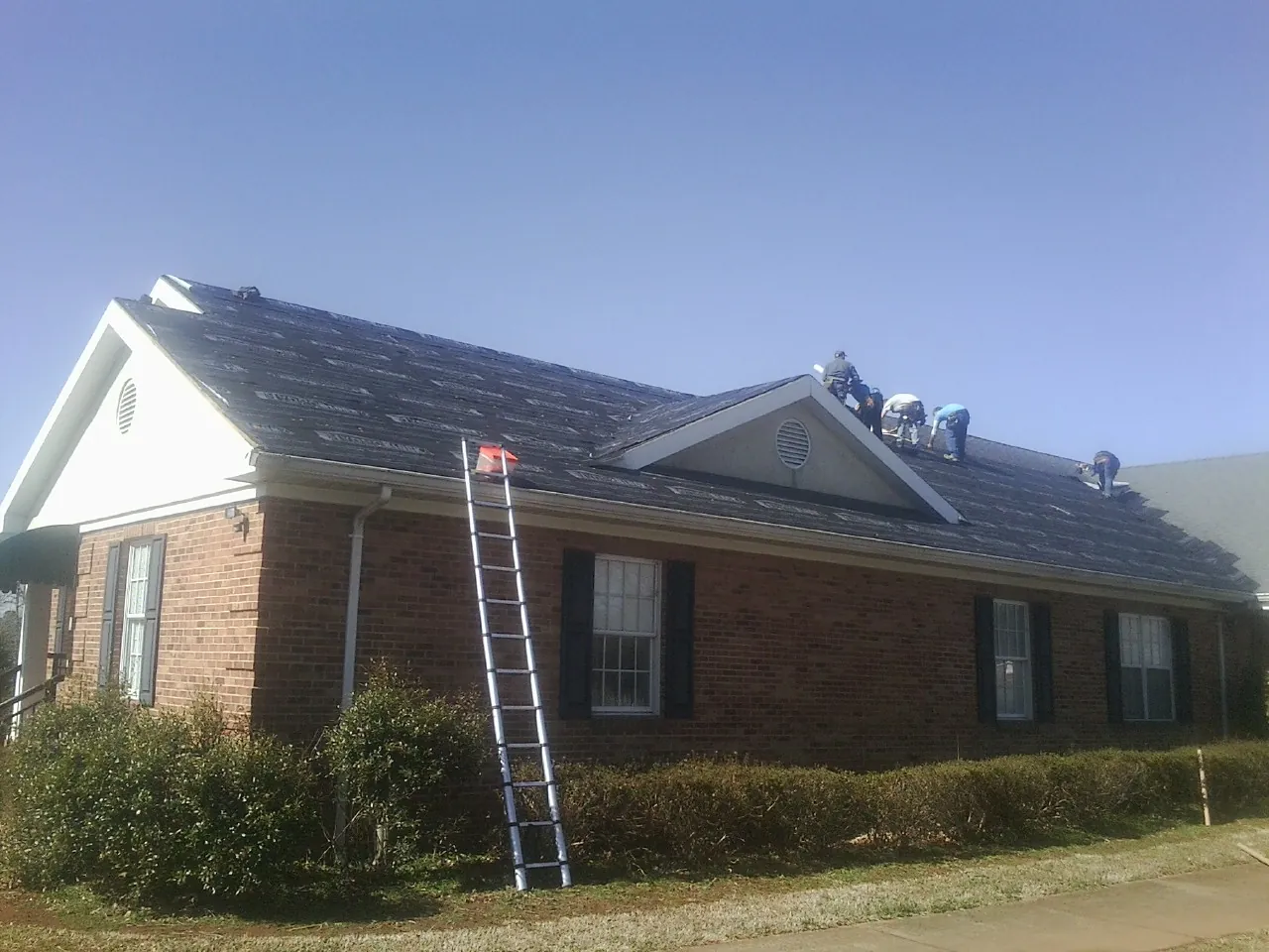 Crew tearing shingles off a brick ranch roof with a ladder set — Emergency Roof Repair work by our crew in Parkville