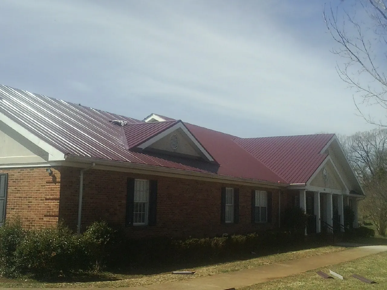 Red metal roof with gabled entries on a long brick building, from a Hail Damage Roof Repair job in Parkville