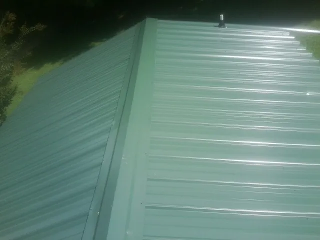 New green metal panels meeting at the ridge of a roof — Flat Roof Repair work by our crew in Parkville