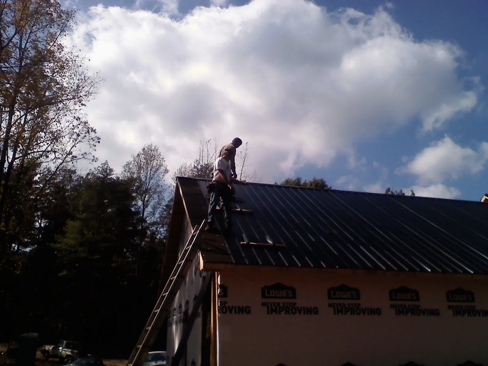 Roofer fastening dark metal panels high against a cloudy sky, from a Roof Inspection job in Parkville