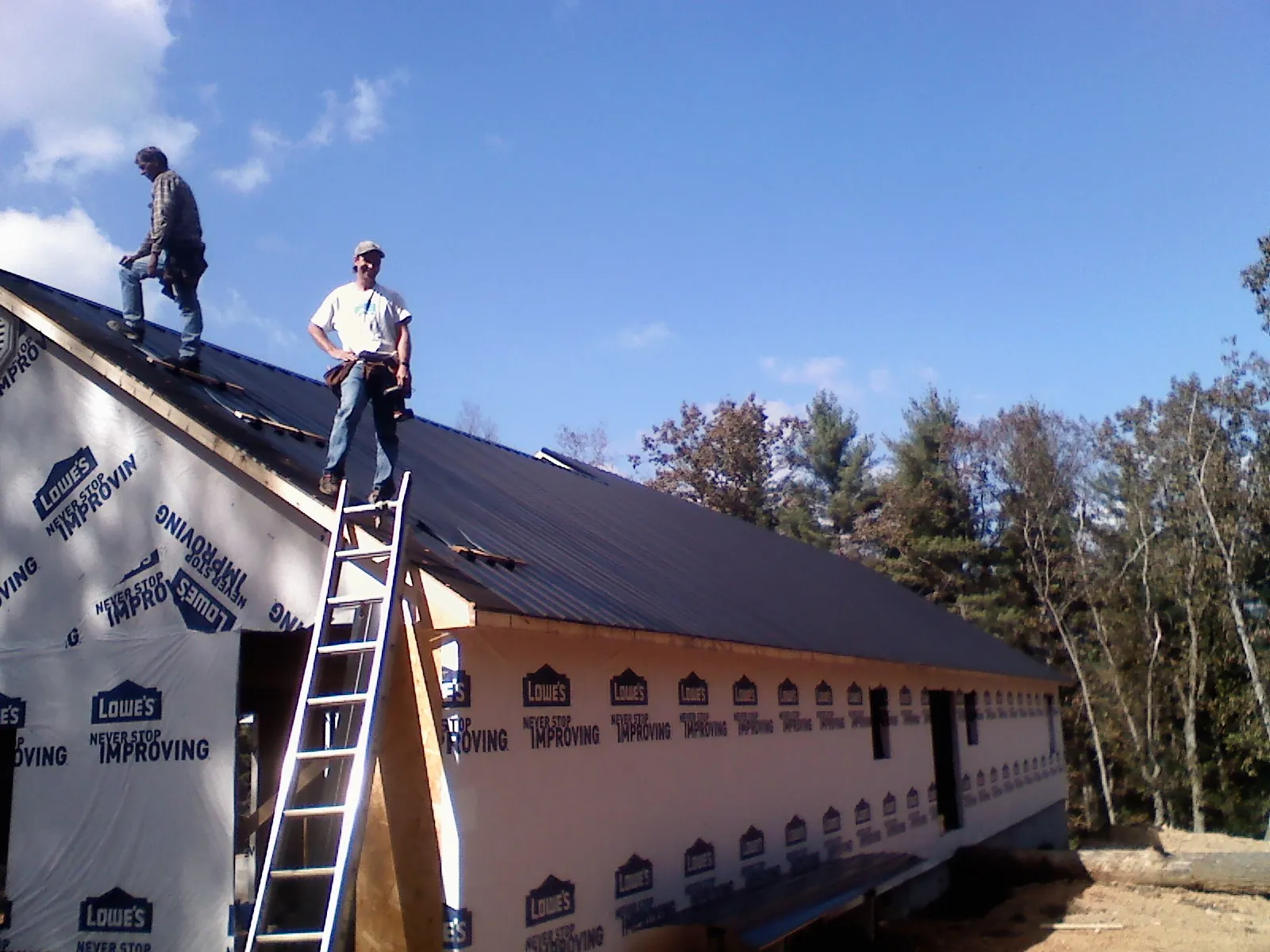Two roofers standing on a long dark metal roof over a wrapped building in Parkville