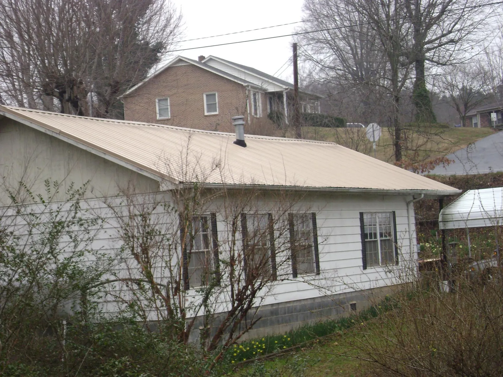 Tan metal roof on a white sided house set into a hillside — Commercial Roofing by Roofing Brothers in Parkville