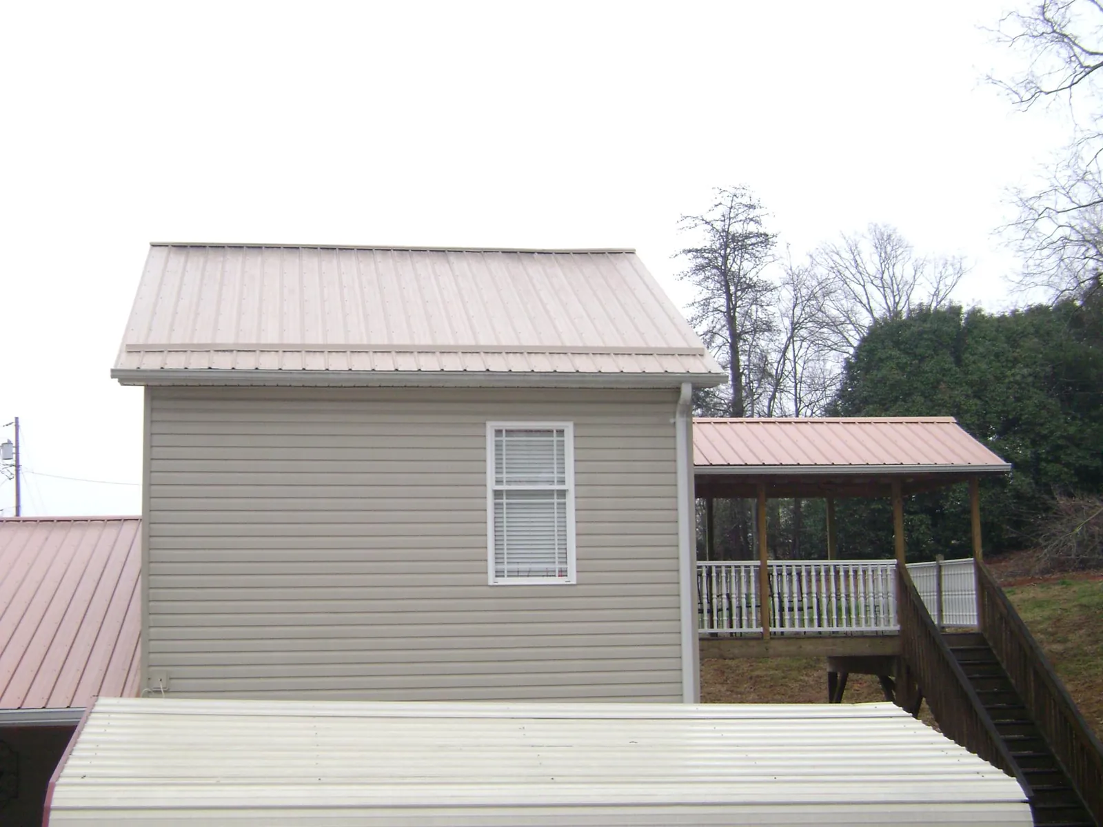 Tan metal roofs on a two story addition and attached porch, from a Roof Replacement job in Parkville