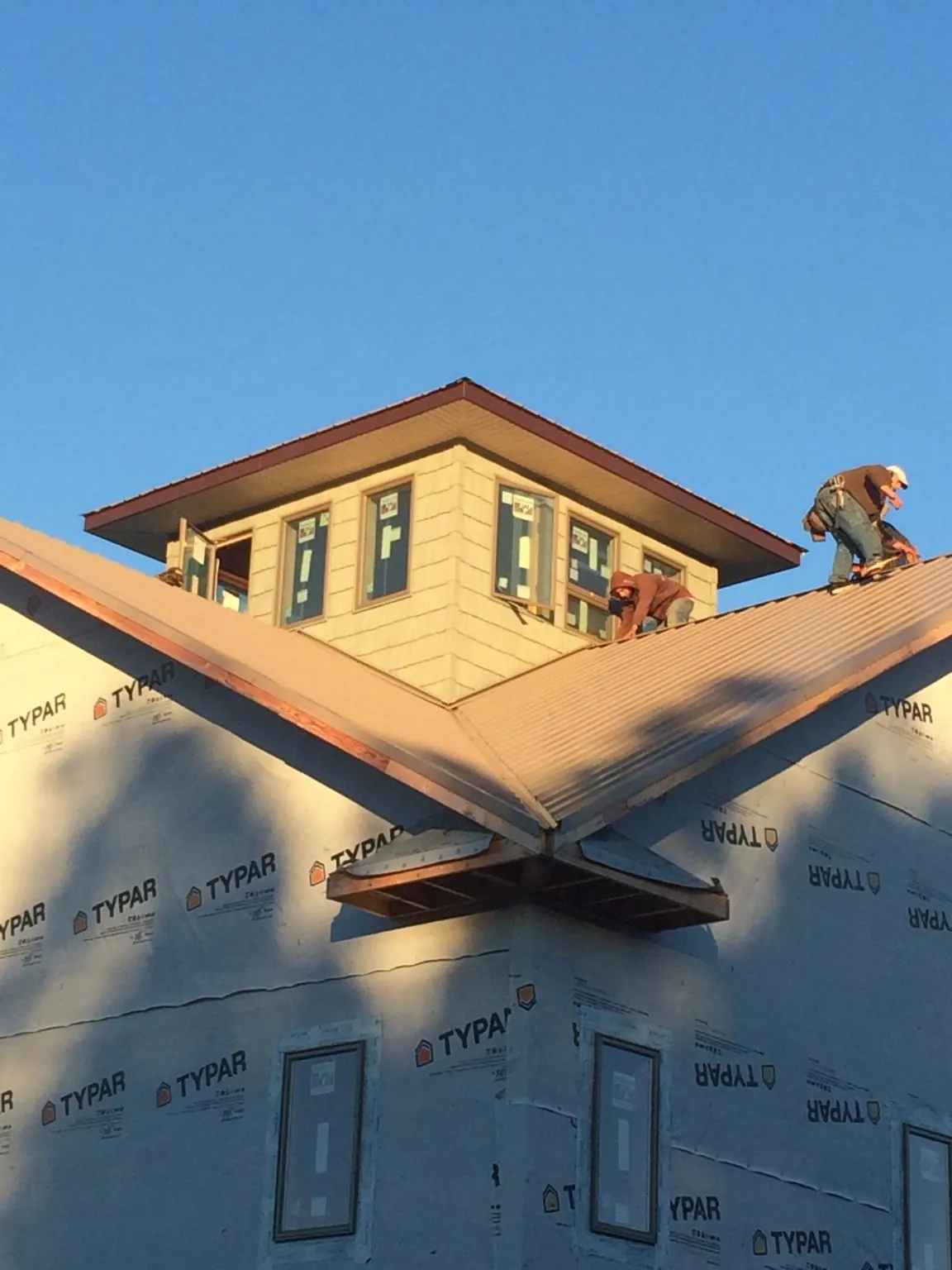 Roofers working around a rooftop cupola on a new metal roof at sunset — Roof Waterproofing in Parkville by Roofing Brothers